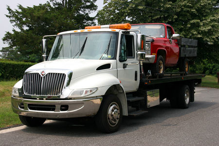 Picture of a flat bed tow truck carrying a pickup truck.